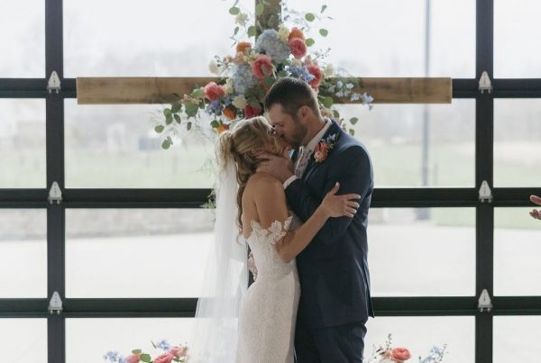 Ashley and Chris share their first kiss in front of a floral wooden cross at The Grange Hall