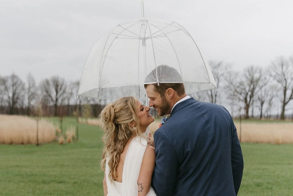 Ashley and Chris under a clear umbrella on a rainy spring day at The Grange Hall