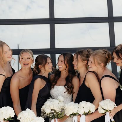 Ava laughing with her bridesmaids in black dresses holding white rose bouquets