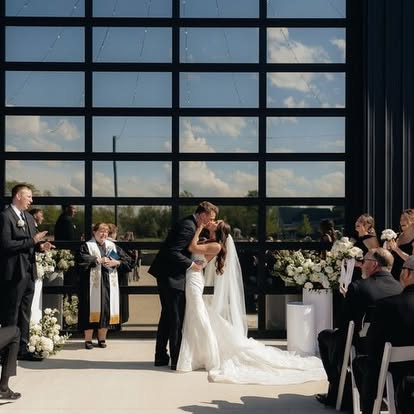 Ava and Carter share their first kiss in front of the glass garage doors at The Grange Hall, surrounded by white florals