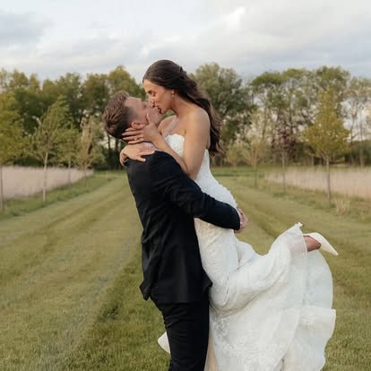 Carter lifts Ava for a kiss on the tree-lined lawn at The Grange Hall