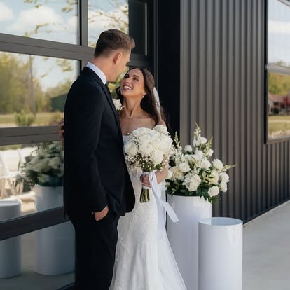 Ava holds a white rose bouquet while smiling up at Carter beside The Grange Hall