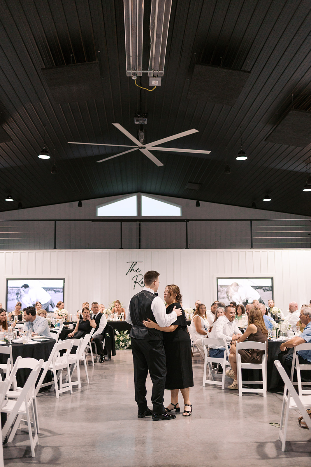 Derek shares a dance with family in the reception hall with black linens and a The Robbs sign