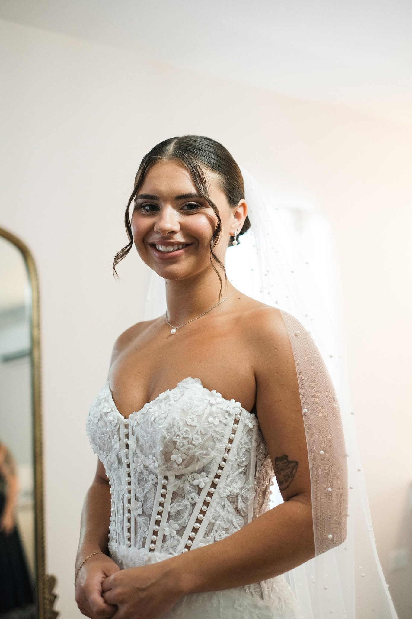 Faith smiling in her strapless lace corset gown and pearl veil in the bridal suite
