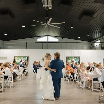 Faith and George share their first dance in The Grange Hall reception space as guests look on