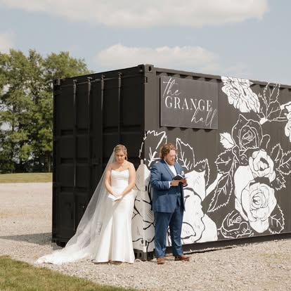 Faith and George read letters to each other on either side of The Grange Hall’s floral mural shipping container
