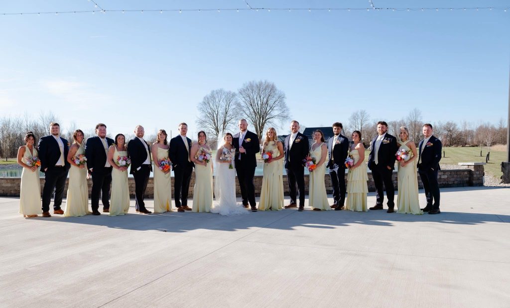 Maddie and Ethan with their bridal party in butter yellow dresses and black suits on the patio at The Grange Hall