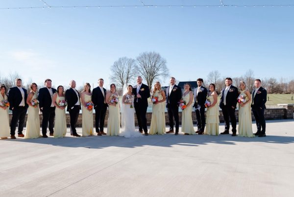 Maddie and Ethan with their bridal party in butter yellow dresses and black suits on the patio at The Grange Hall