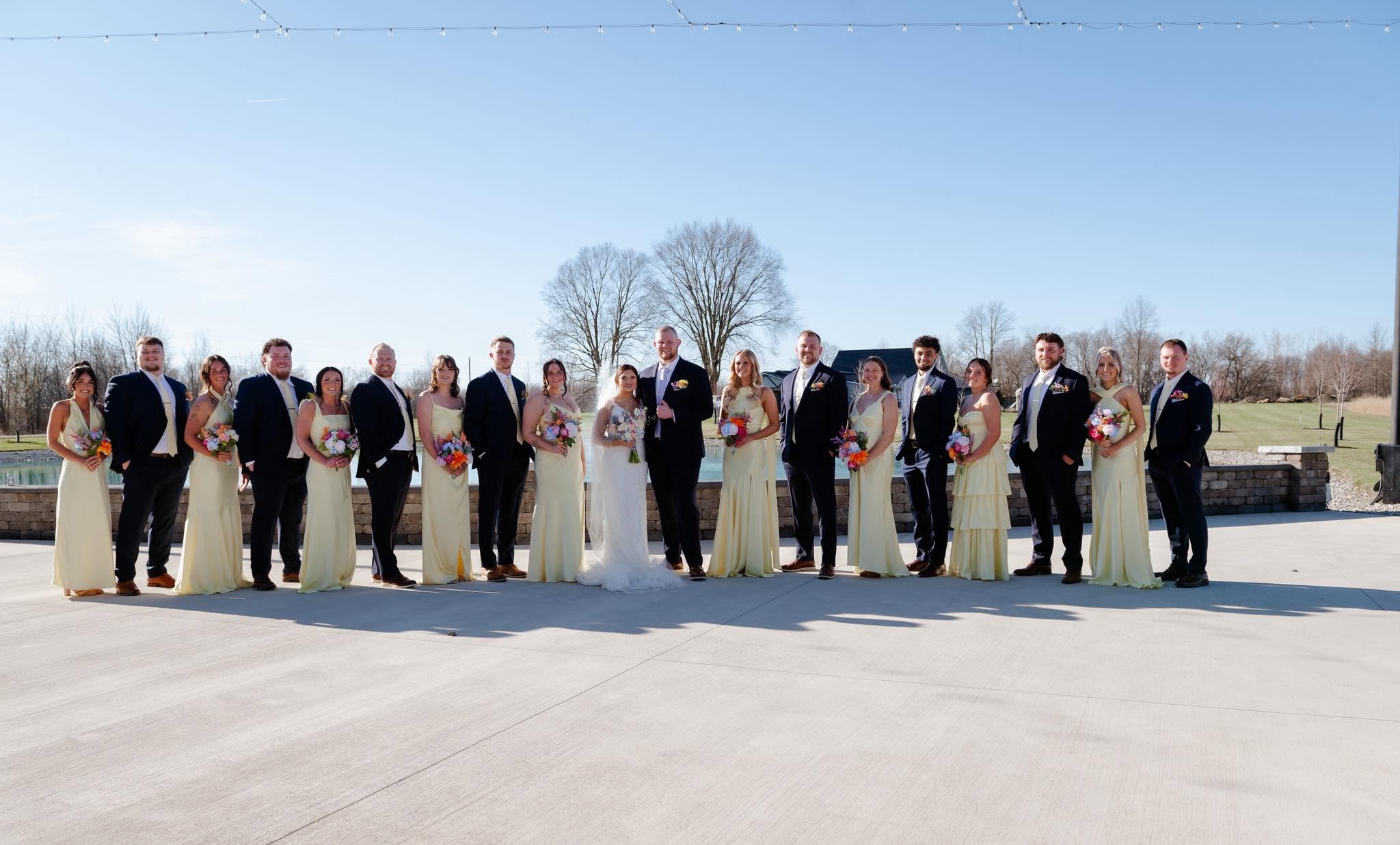 Maddie and Ethan with their bridal party in butter yellow dresses and black suits on the patio at The Grange Hall