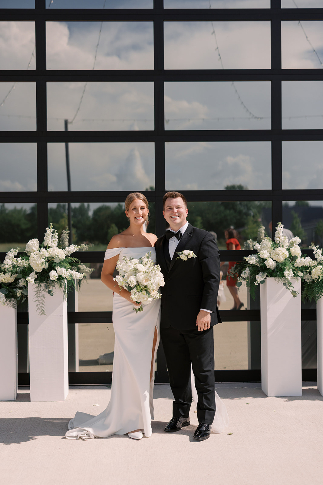 Taylor and Derek smiling in front of the glass garage doors flanked by white floral pedestals after their ceremony