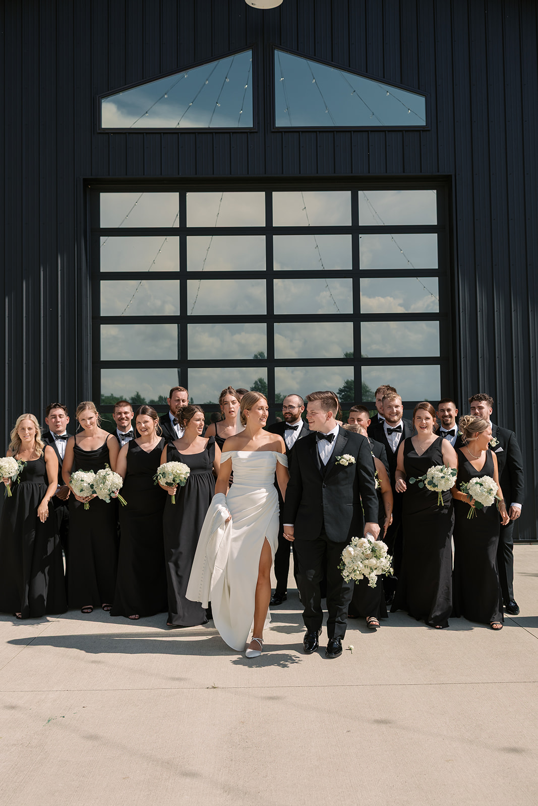 Taylor and Derek walk hand in hand in front of their wedding party in black gowns and tuxedos